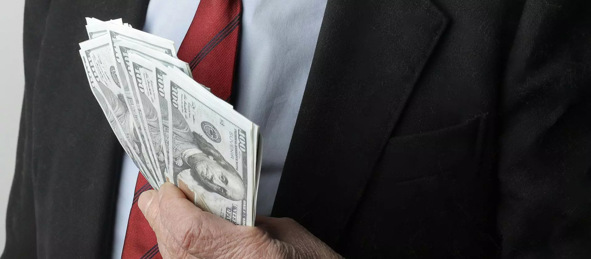A man in a suit holds a large amount of US dollars in his hand
